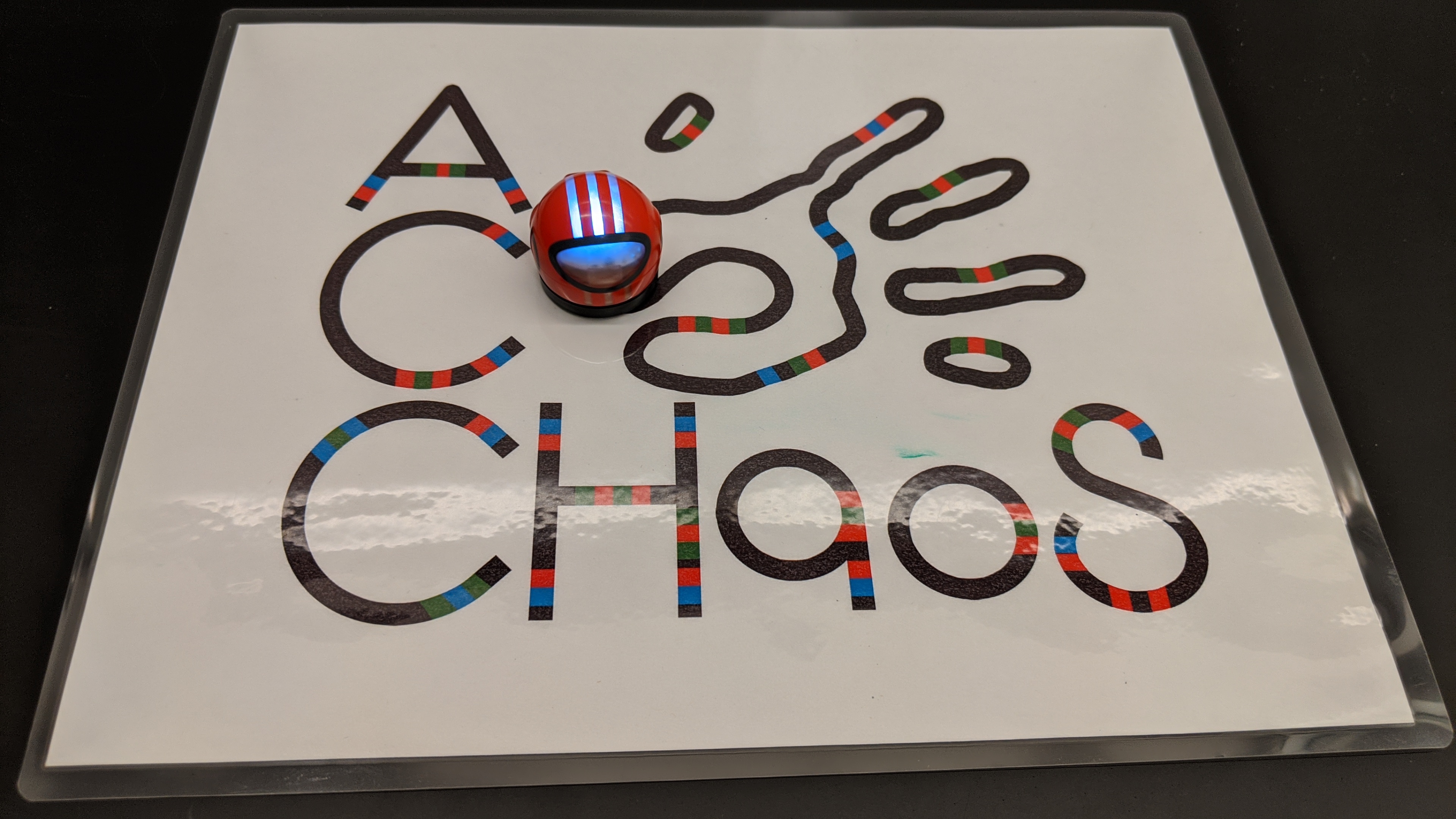 A small spherical robot moves along a picture of the ACCHaoS logo