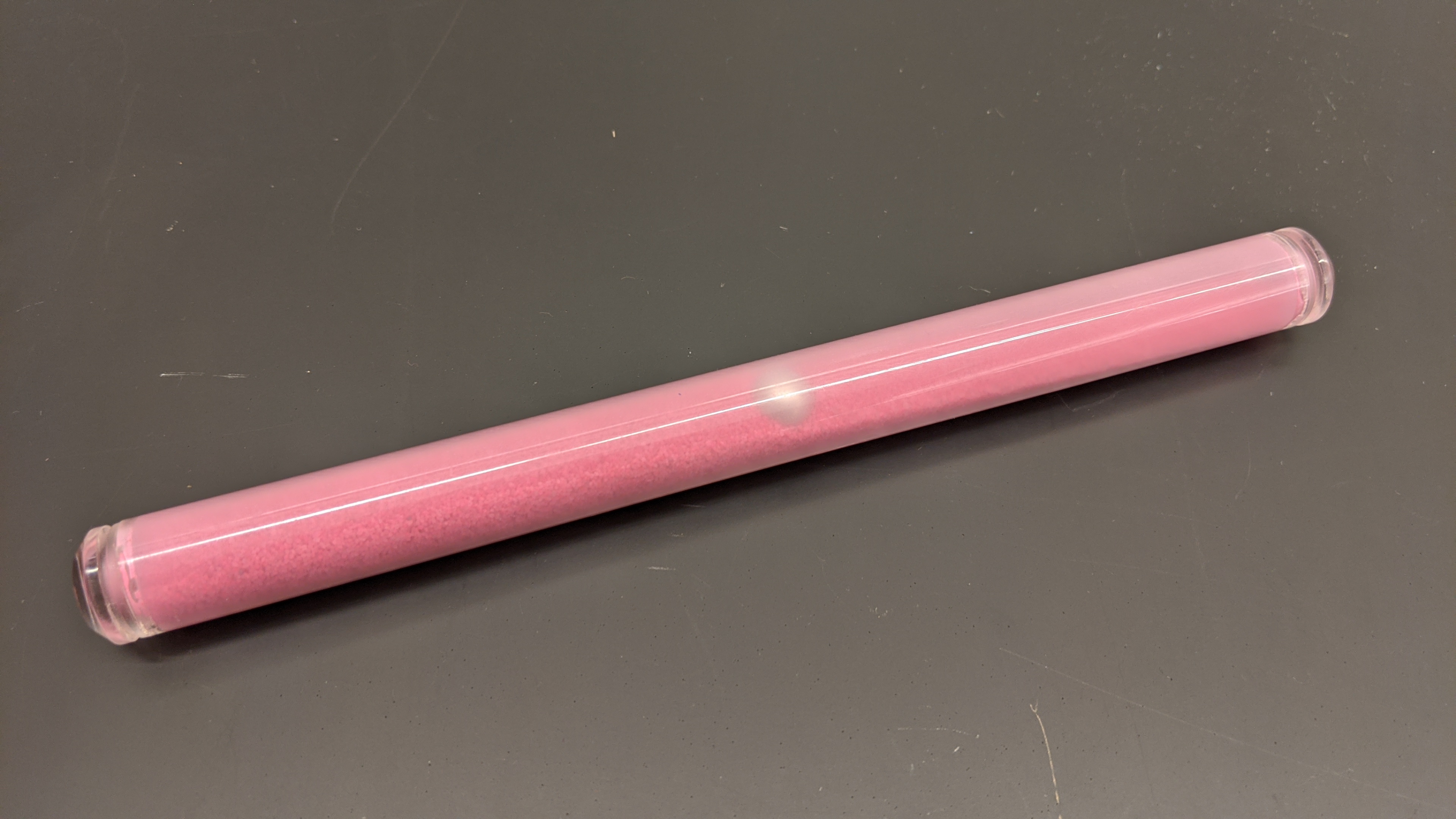 A clear plastic tube with pink sand and a metal sphere inside