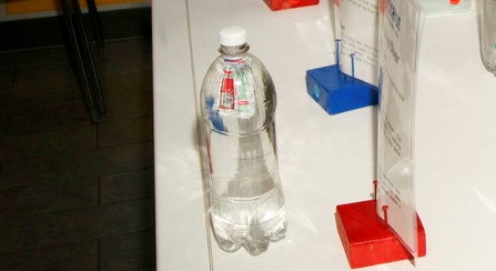 A ketchup packet floats at the top of a plastic 1L bottle filled with water.