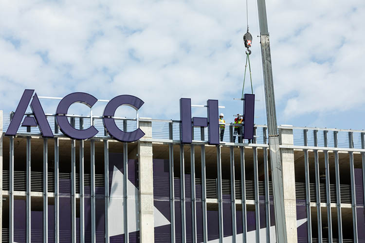 A crane lowers a large letter I next to the letters that will spell, ACC HIGHLAND, onto the East facing side of the Highland Campus parking garage.