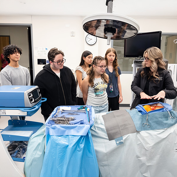 Austin Community College | Austin Community College District A group students gather around a medical dummy as an instructor wearing an ACC jacket demonstrates surgical instruments and procedures in the medical simulation center at ACC Highland campus.