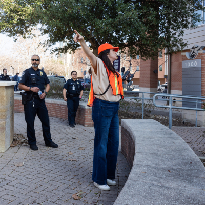 Austin Community College | Austin Community College District A woman wearing a safety vest directs students in a safety drill at Austin Community College while two campus police officers, a man and a woman, look on.