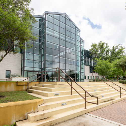 a photo of a glass fronted office building facing stone steps with two railings and trees and grass off to the sides.