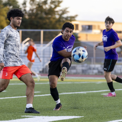 Austin Community College | Austin Community College District An ACC Riverbat soccer player in purple kicks a soccer ball as a defender in a grey jersey and orange shorts tries to defend, and another Riverbat player in purple runs up from behind.
